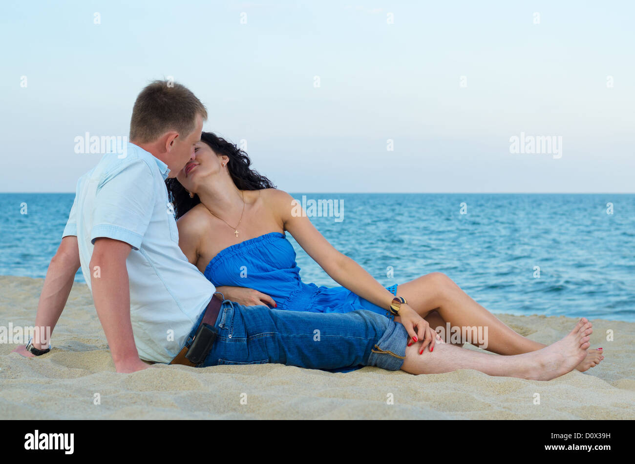 Loving couple reclining on a sandy beach kissing in front of the ocean Stock Photo