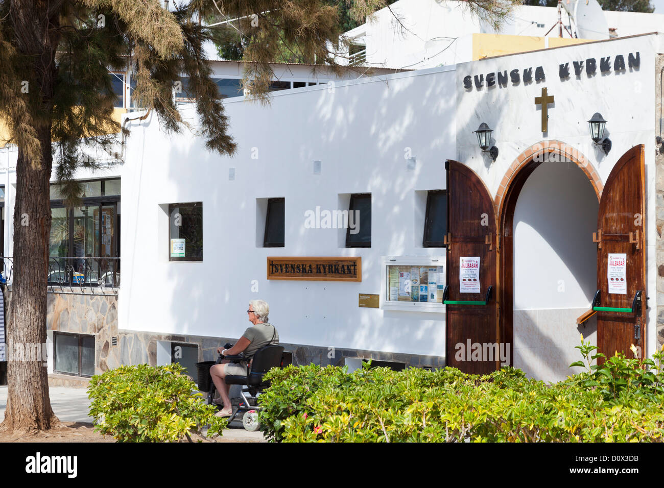 A woman in a motorised whelchair passing the Scandanavian church in los Cristianos, Tenerife, Canary Islands, Spain. Stock Photo