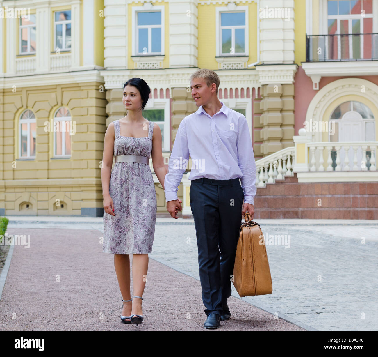 Elegant young couple on vacation walking hand in hand along a sidewalk in an affluent urban environment Stock Photo