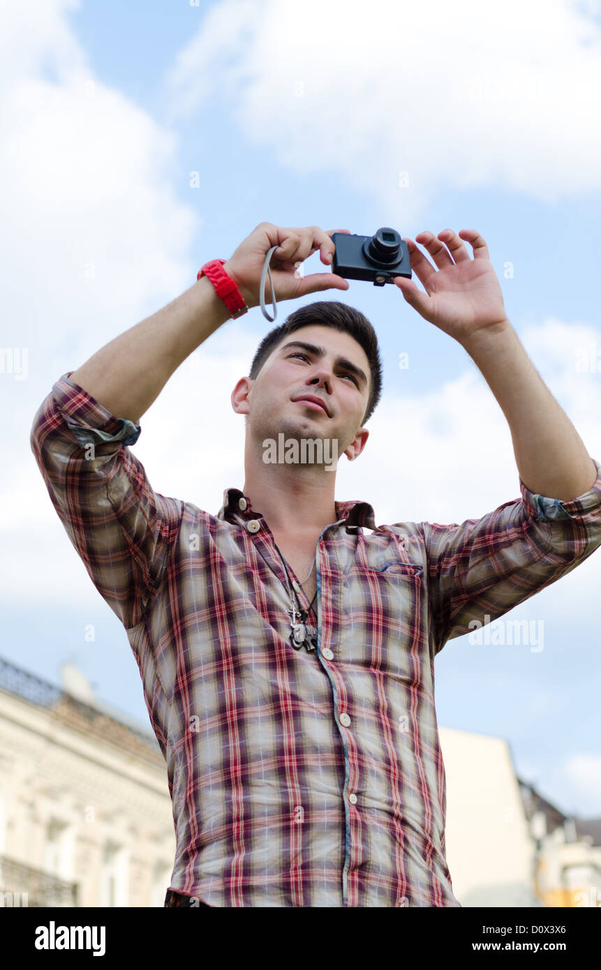 Low angle view of a young man taking a photograph with a compact camera against a cloudy blue sky Stock Photo