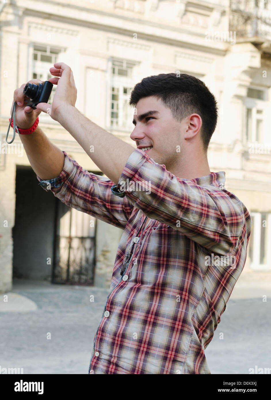 Smiling young man standing outdoors in an urban environment taking a photograph Stock Photo
