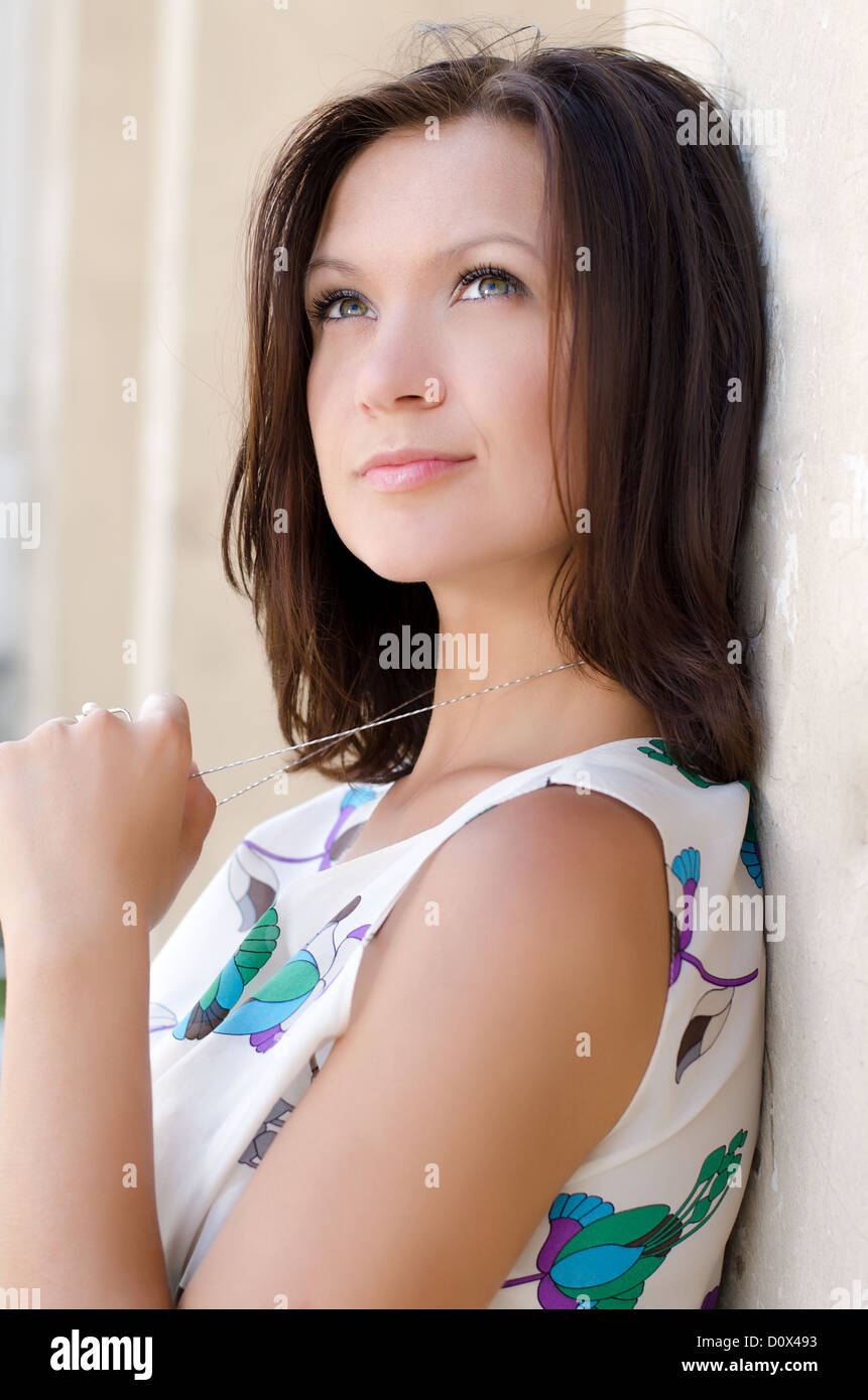 Young woman daydreaming and twiddling her necklace while relaxing leaning back against a building wall Stock Photo