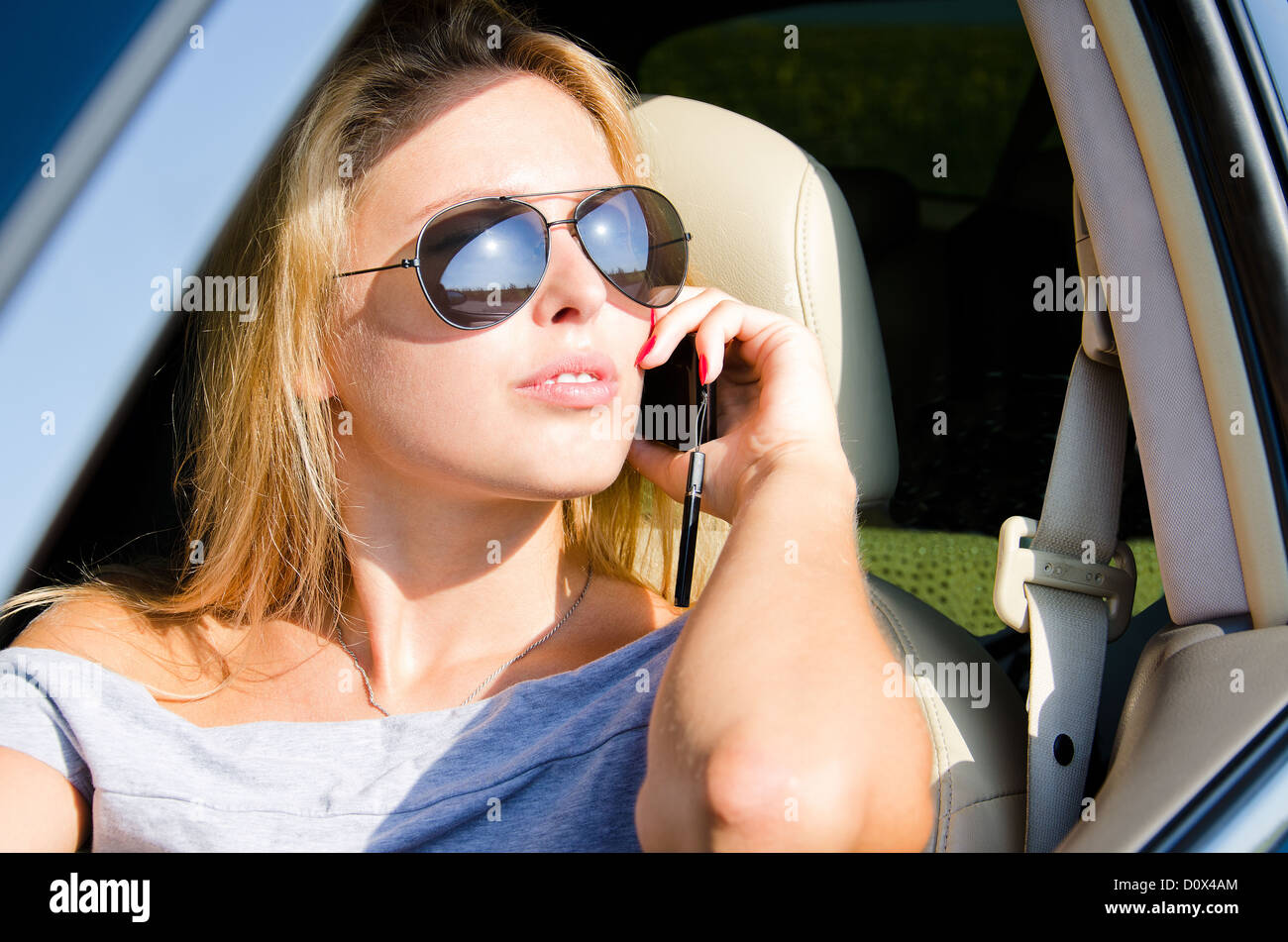 View through the open side window of a beautiful woman in sunglasses using a mobile in her car Stock Photo
