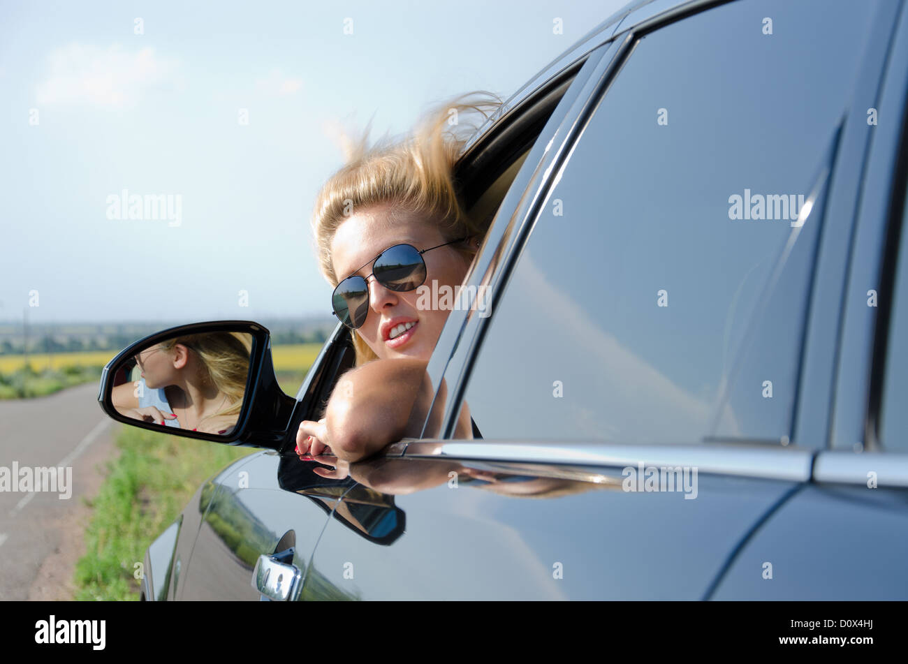 Attractive blonde woman wearing sunglasses leaning out looking back out of a car window Stock Photo