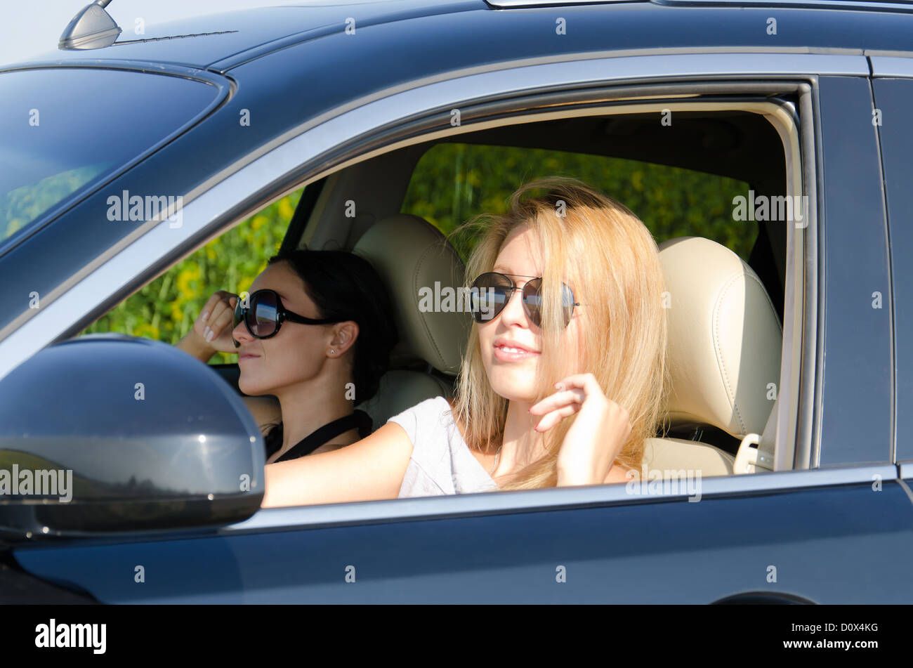 Two beautiful women siting in a luxury car with one looking out through an open window Stock Photo