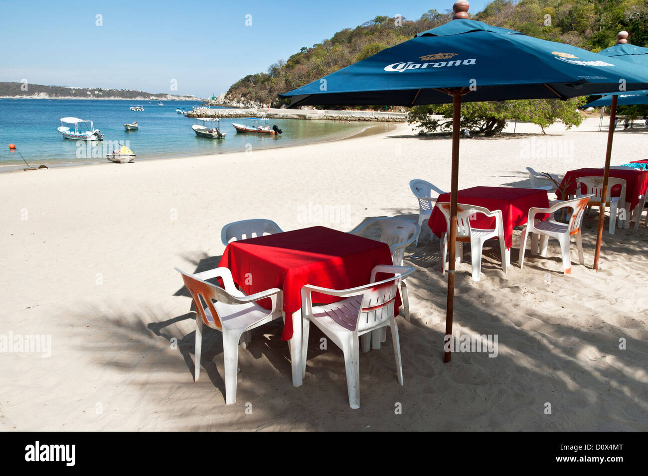 tables shaded by umbrellas line the periphery of white sand beach overlooking sheltered cove at playa La Entrega Huatulco Mexico Stock Photo