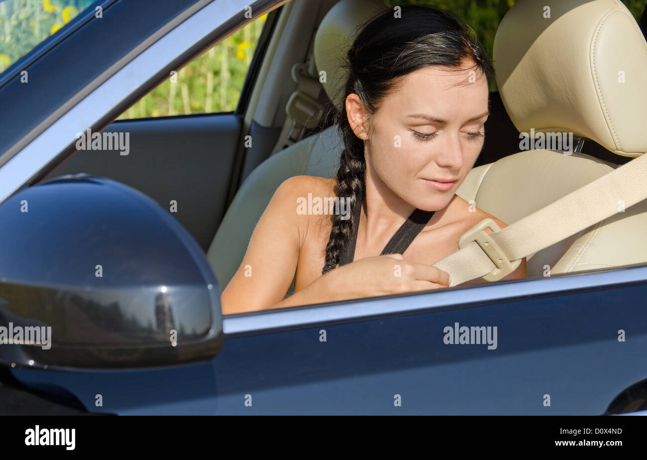 Woman sitting in a car reaching behind her to put on her seatbelt before commencing her journey Stock Photo