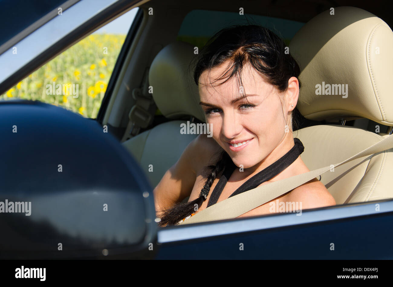 Beautiful smiling young woman wearing a seatbelt seated in a motor car looking out of the window Stock Photo