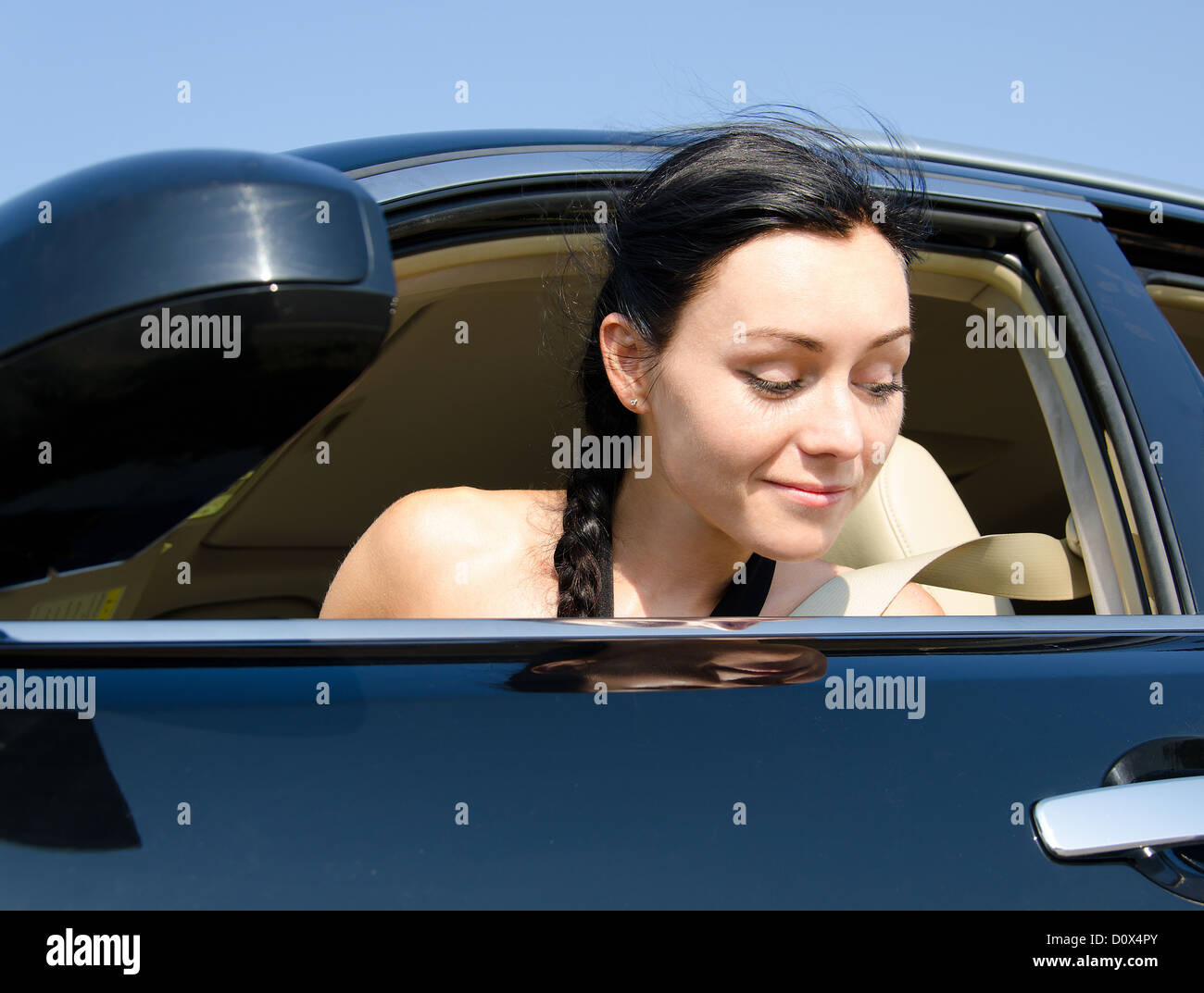 Woman looking out of her car window peering down at the ground with a smile on her face Stock Photo