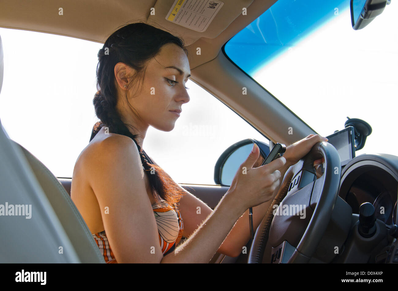 Woman driver sitting behind the steering wheel reading a text message on a mobile Stock Photo