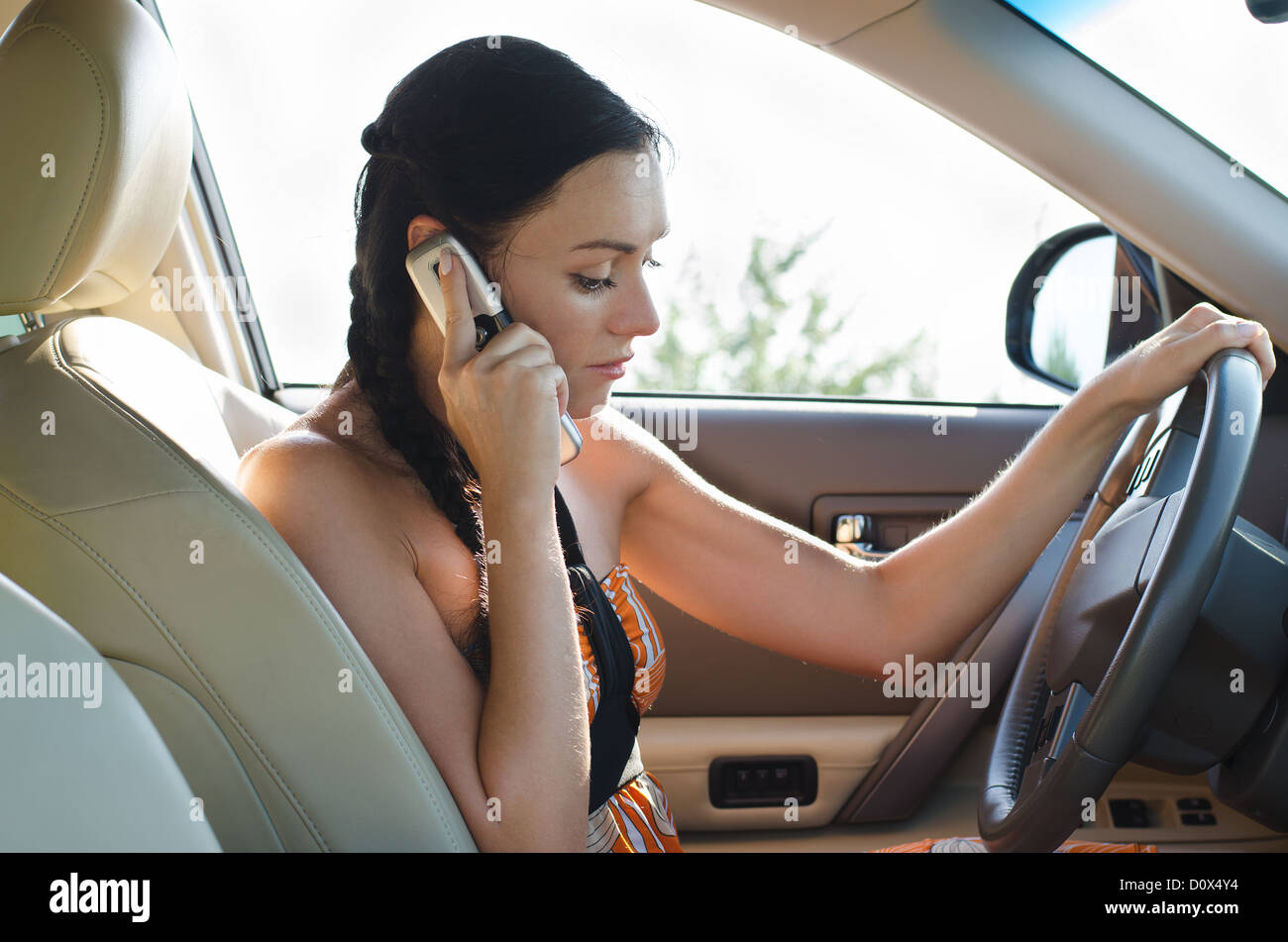 Beautiful young girl sitting in the drivers seat in car chatting on her mobile Stock Photo