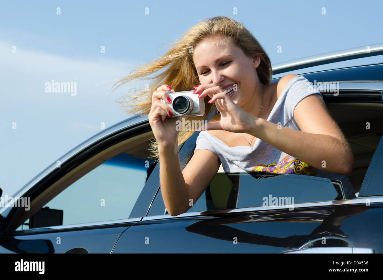 Laughing woman taking digital photographs leaning out of the rear passenger window of a motor car Stock Photo