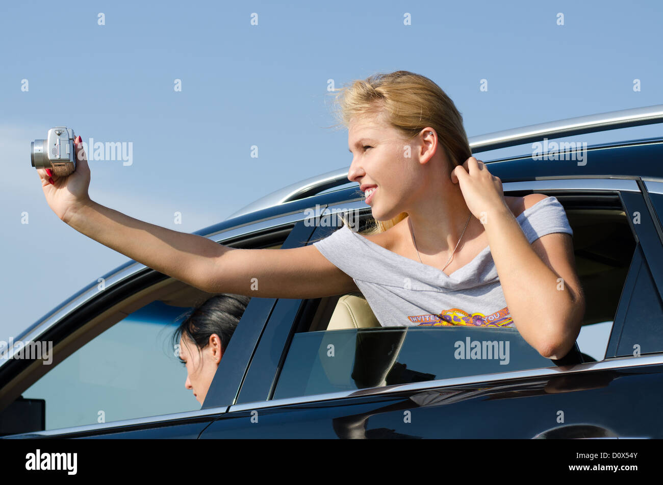 Young blonde woman leaning out of the passenger window taking photos from a car Stock Photo