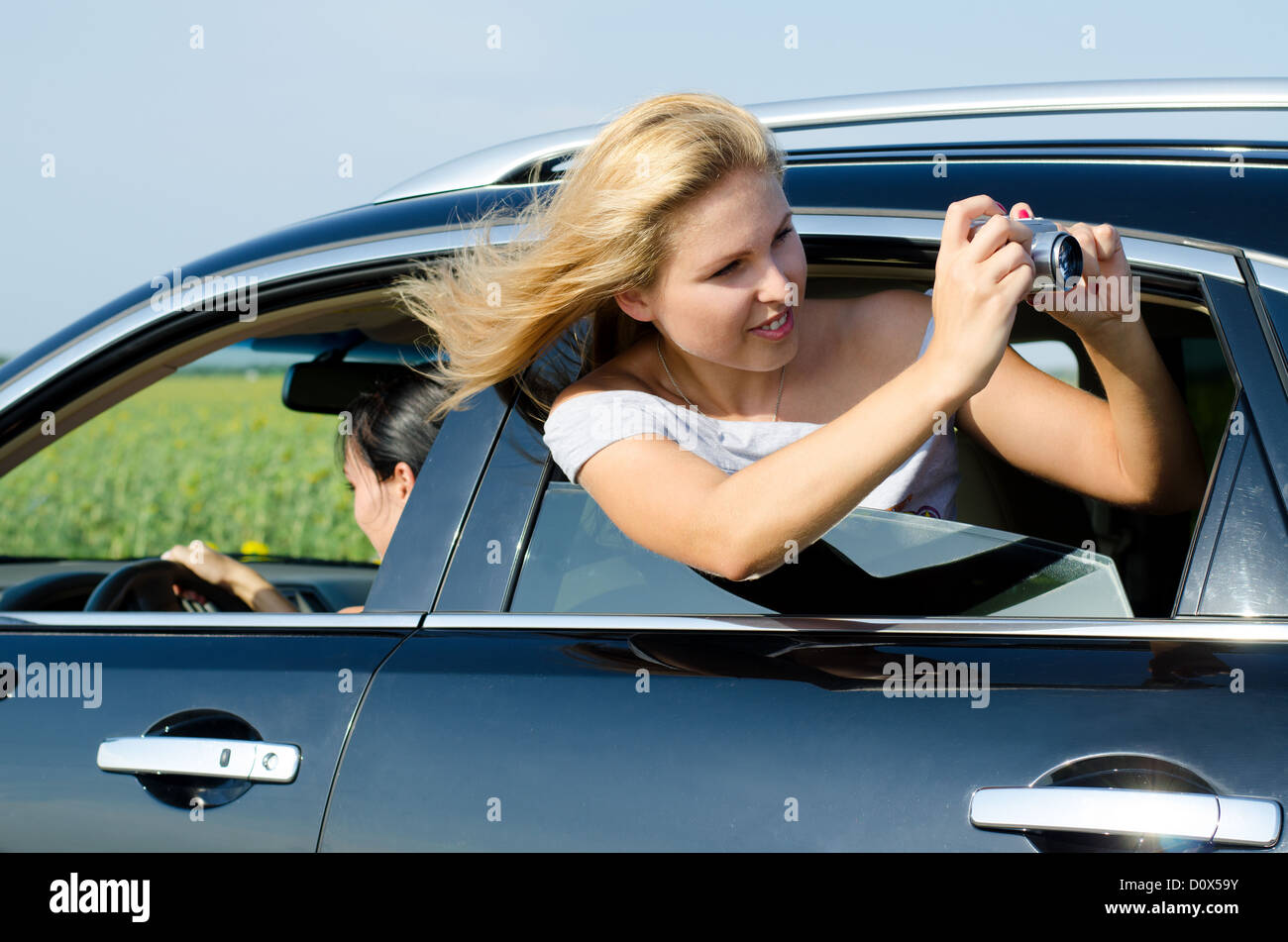 Attractive woman leaning out and photographing from the open rear car window with her hair blowing in the breeze Stock Photo