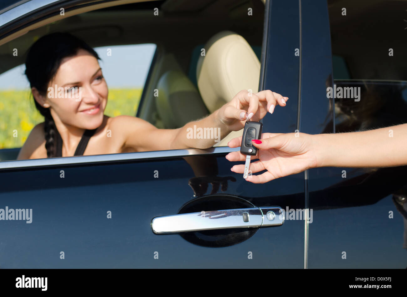 Smiling driver holding her car key out of the window of the vehicle towards a second womans outstretched hand Stock Photo