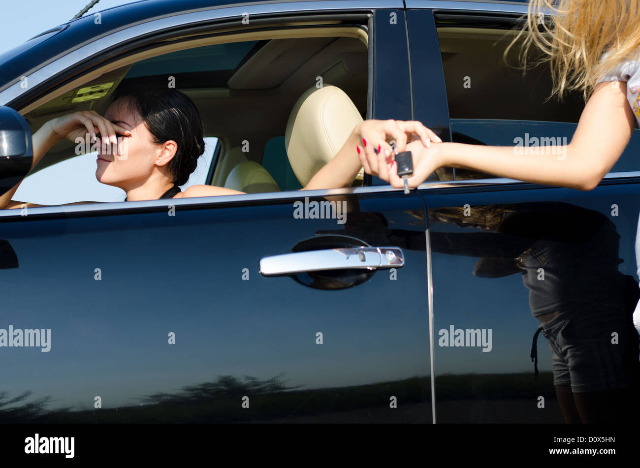 Tired woman driver with her hand to her head handing over her car keys to a second woman to take over Stock Photo