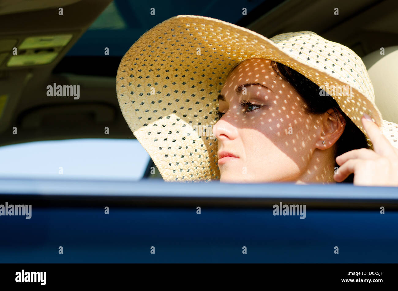 Beautiful woman in a wide brimmed straw hat protecting her eyes from the sunlight sitting in a car Stock Photo