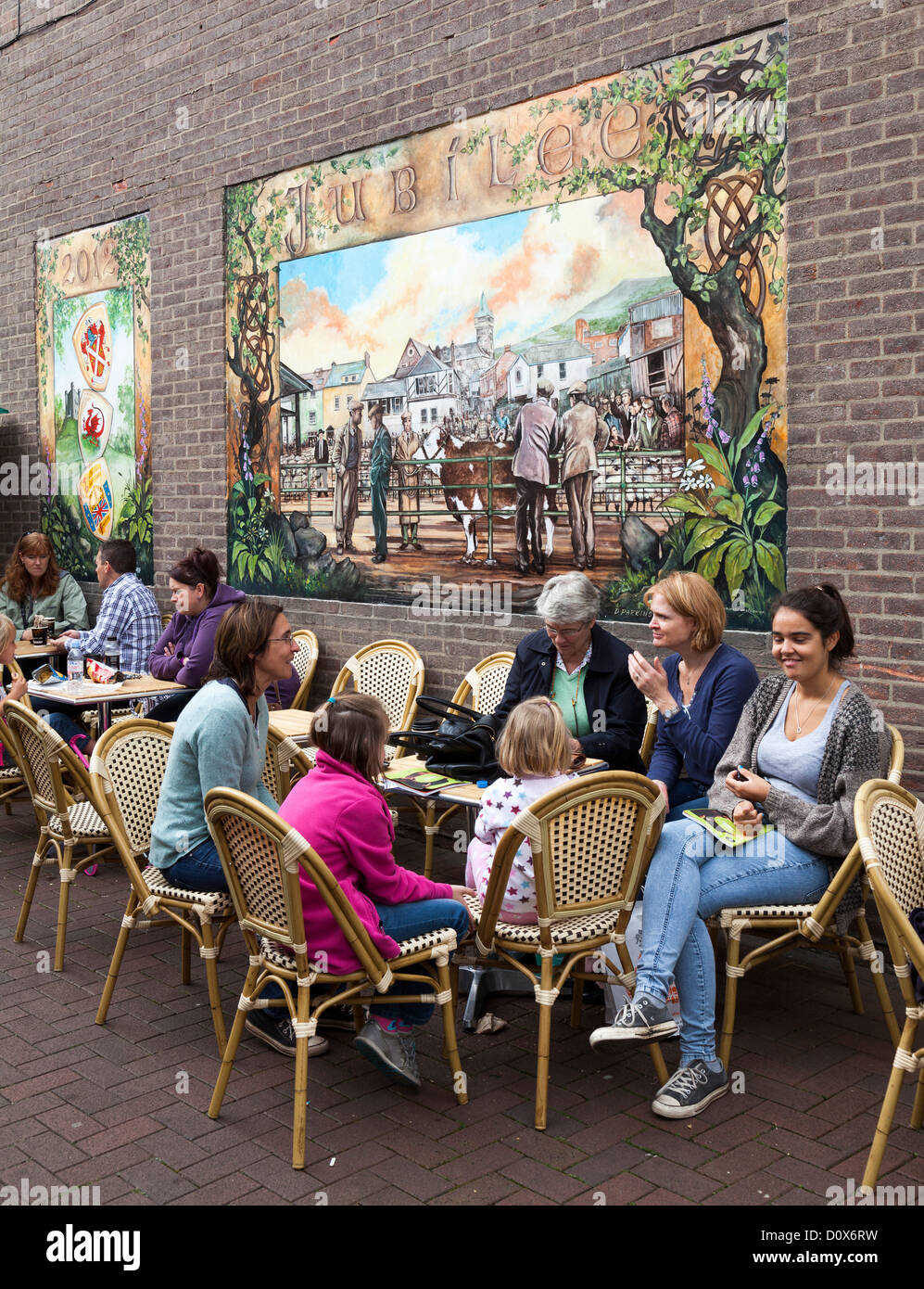 People eating at tables outdoors in street with mural of cattle market