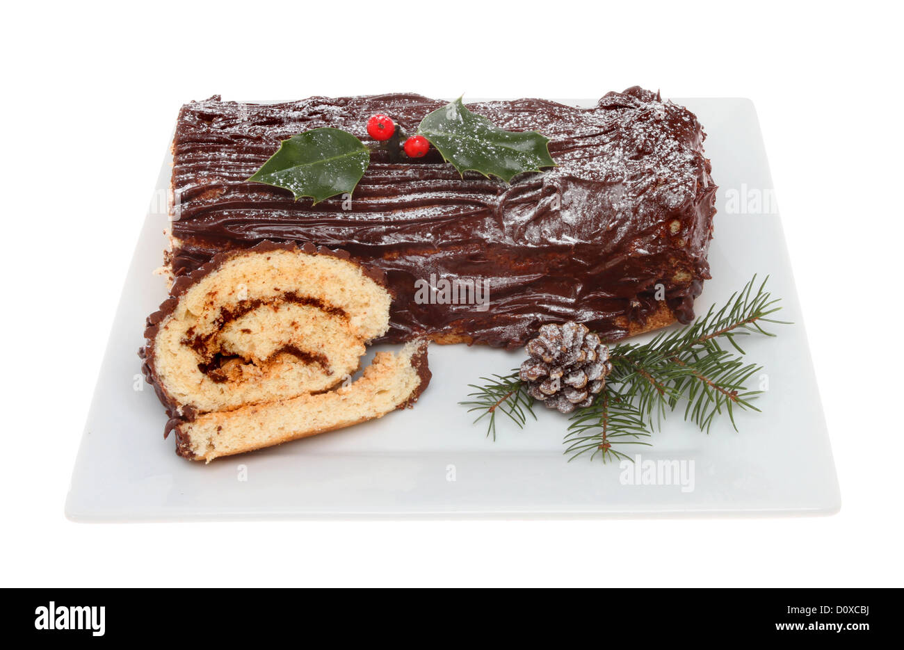 Chocolate yule log on a plate decorated with holly and seasonal foliage isolated against white Stock Photo