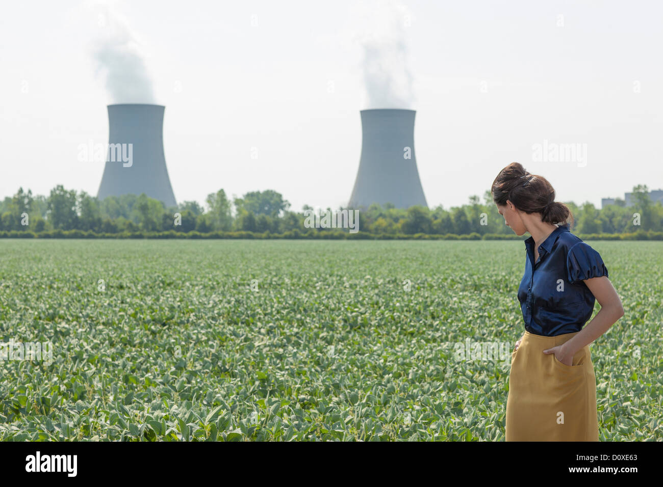 Woman in soy bean filed looking behind to nuclear power station Stock Photo