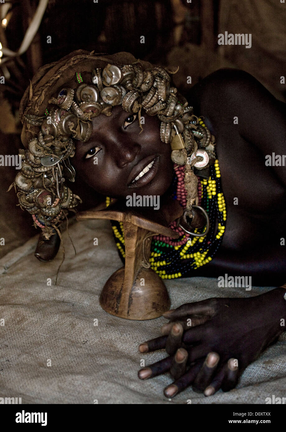 Portrait Of A Dassanech Tribe Girl With Wig Made Of Caps Using Headrest To Lay Down, Omorate, Omo Valley, Ethiopia Stock Photo