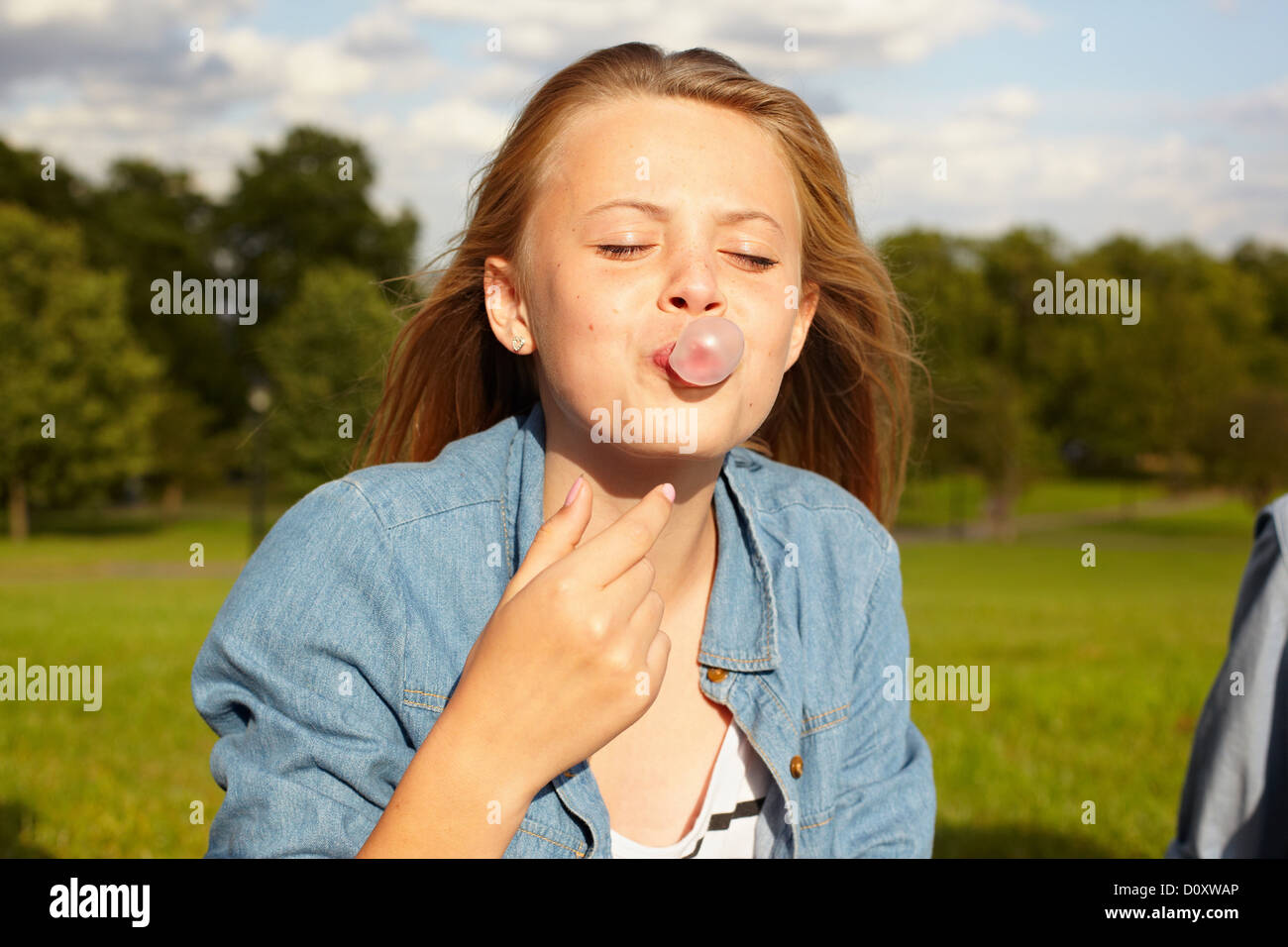Teenage girl in park, blowing bubble gum Stock Photo