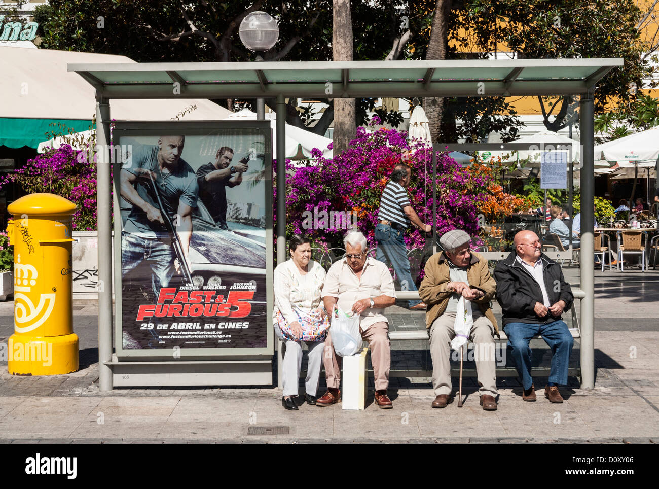 Elderly Spanish people at bust stop alongside Fast and Furios 5 film poster Stock Photo