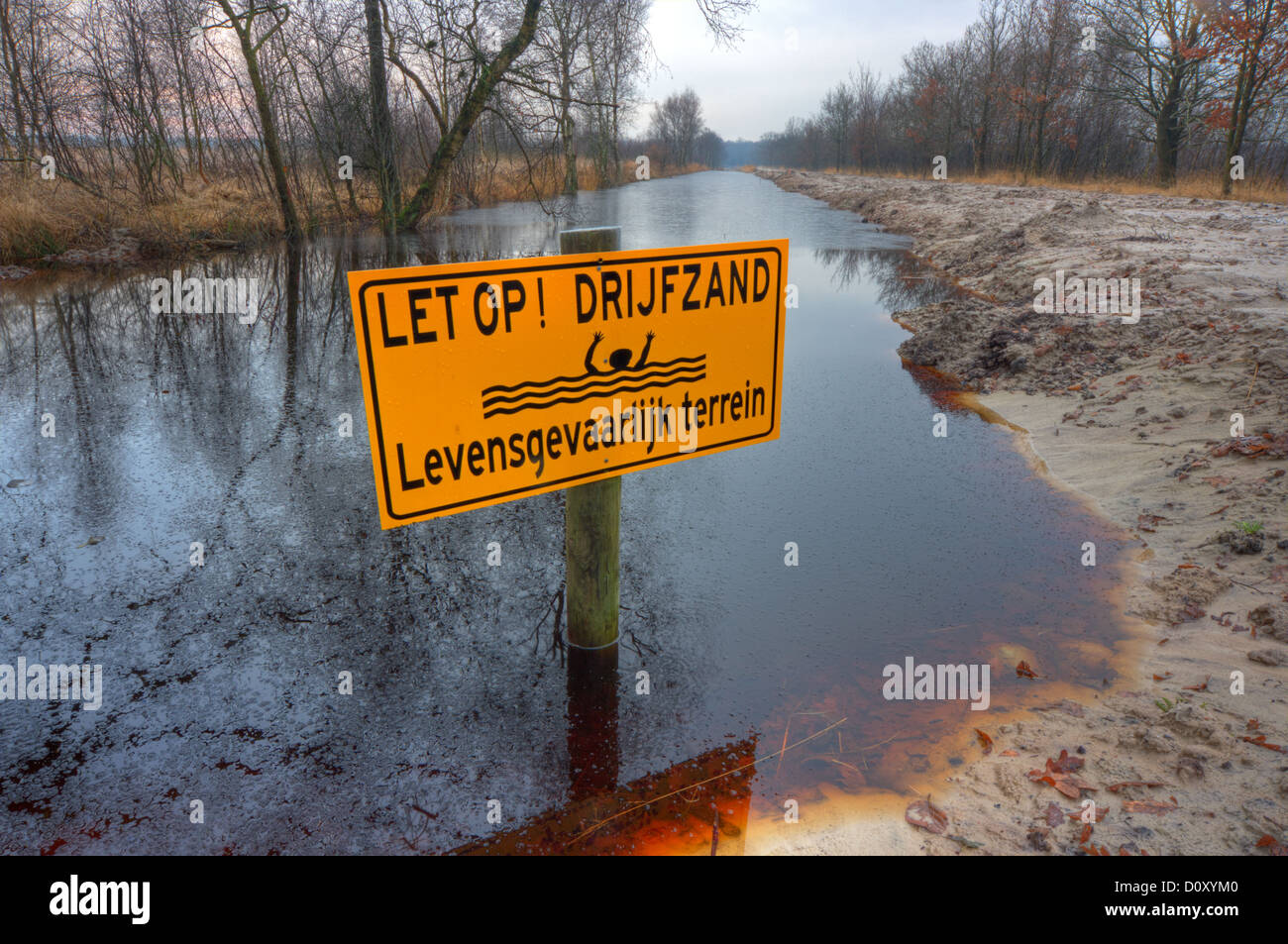 A signboard with the dutch text 'Let op! Drijfzand. Levensgevaarlijk terrein', meaning 'Caution! Quicksand. Dangerous terrain' Stock Photo