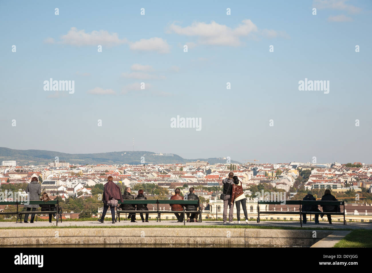 In the Schönbrunn Gardens tourist couples and friends sit, take photos, look out over the city of Vienna beneath hazy blue sky. Stock Photo