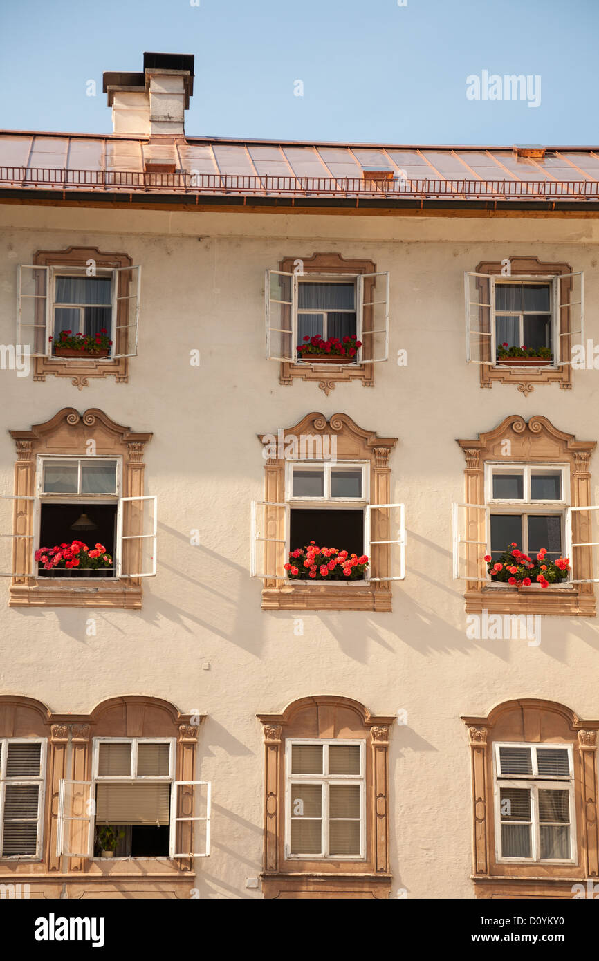 Old multistory yellow residential building in Salzburg with ornately decorative windows, red flower boxes, and a copper roof. Stock Photo