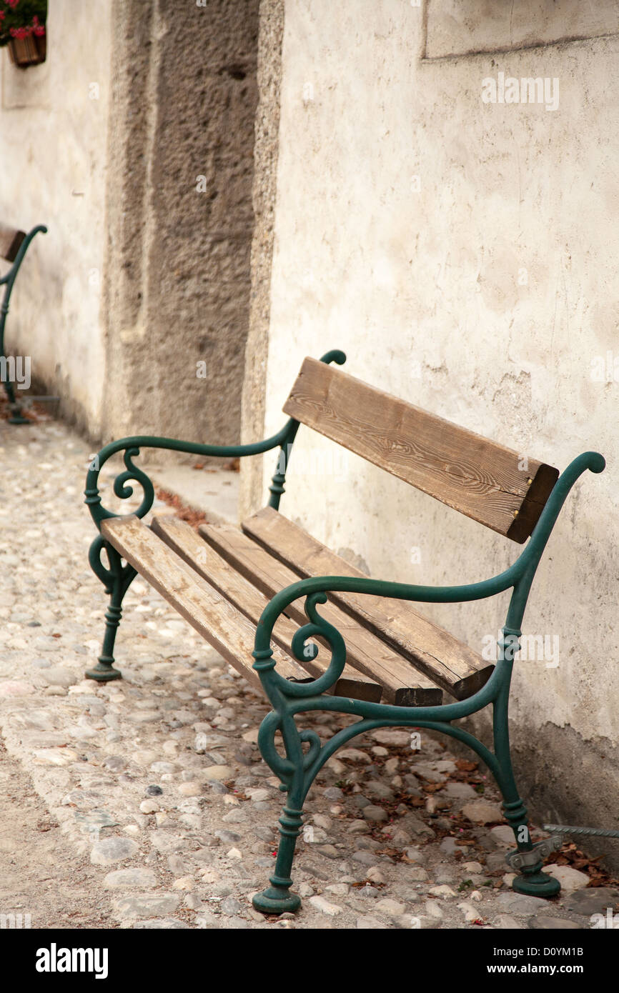 Wooden bench seat sitting on old cobblestones against thick stone wall inside the central courtyard at Festung Hohensalzburg. Stock Photo