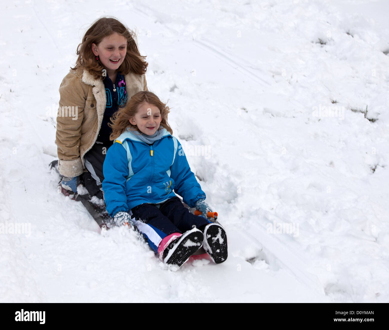 Two young girls sliding down a hill in the snow on a sled Stock Photo