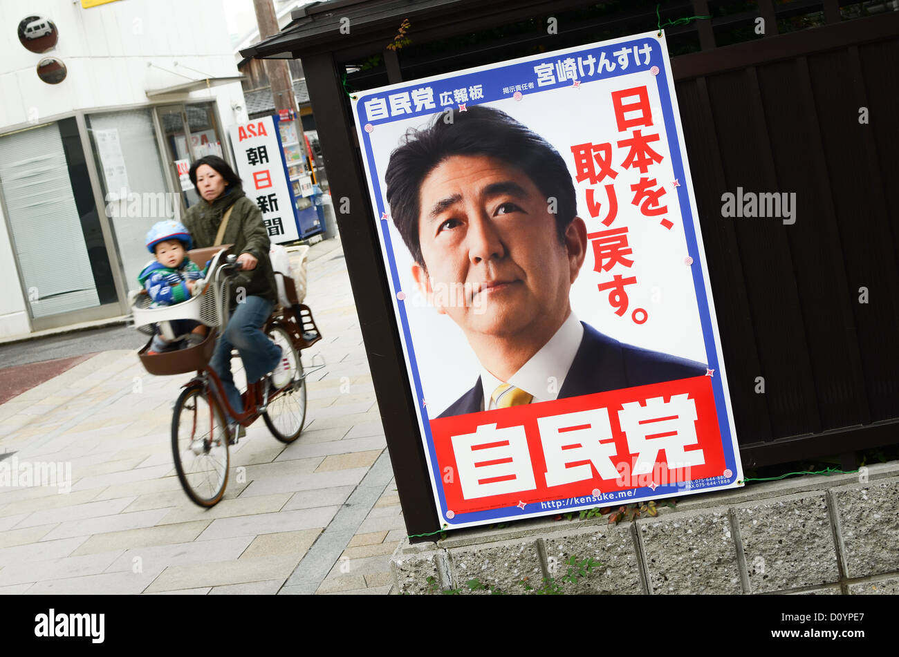 Kyoto, Japan. 4th December 2012. A woman and her child cycle past a campaign poster showing Shinzo Abe, the leader of Japan's main opposition party, the LDP (Liberal Democratic Party). Campaigning kicks off this week for Japan's general election on 16th December, 2012 Credit:  Trevor Mogg / Alamy Live News Stock Photo