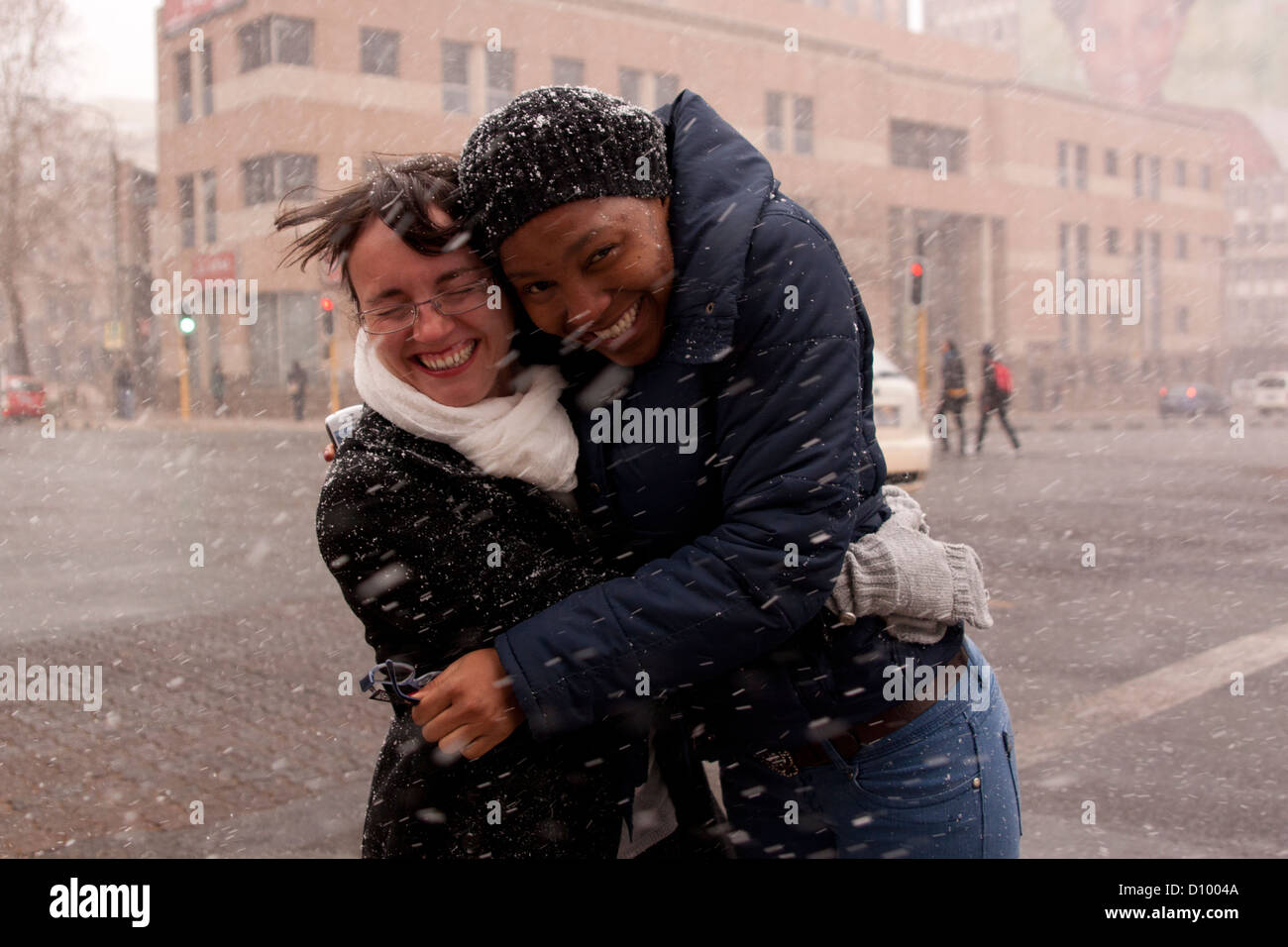Two women holding each other happy while snow falls in city street