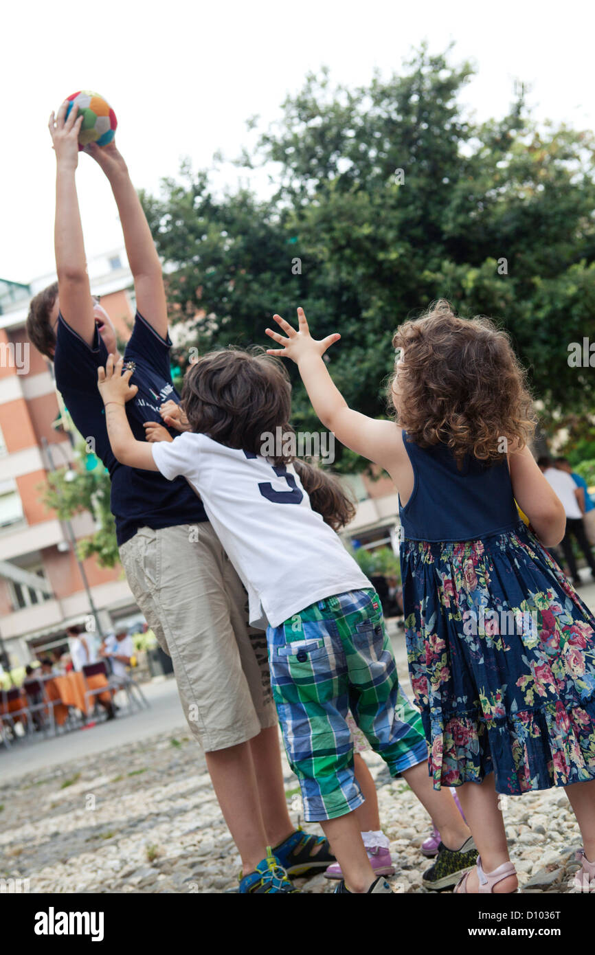 kids trying to reach  soft ball held by a bigger boy playing in the street Stock Photo