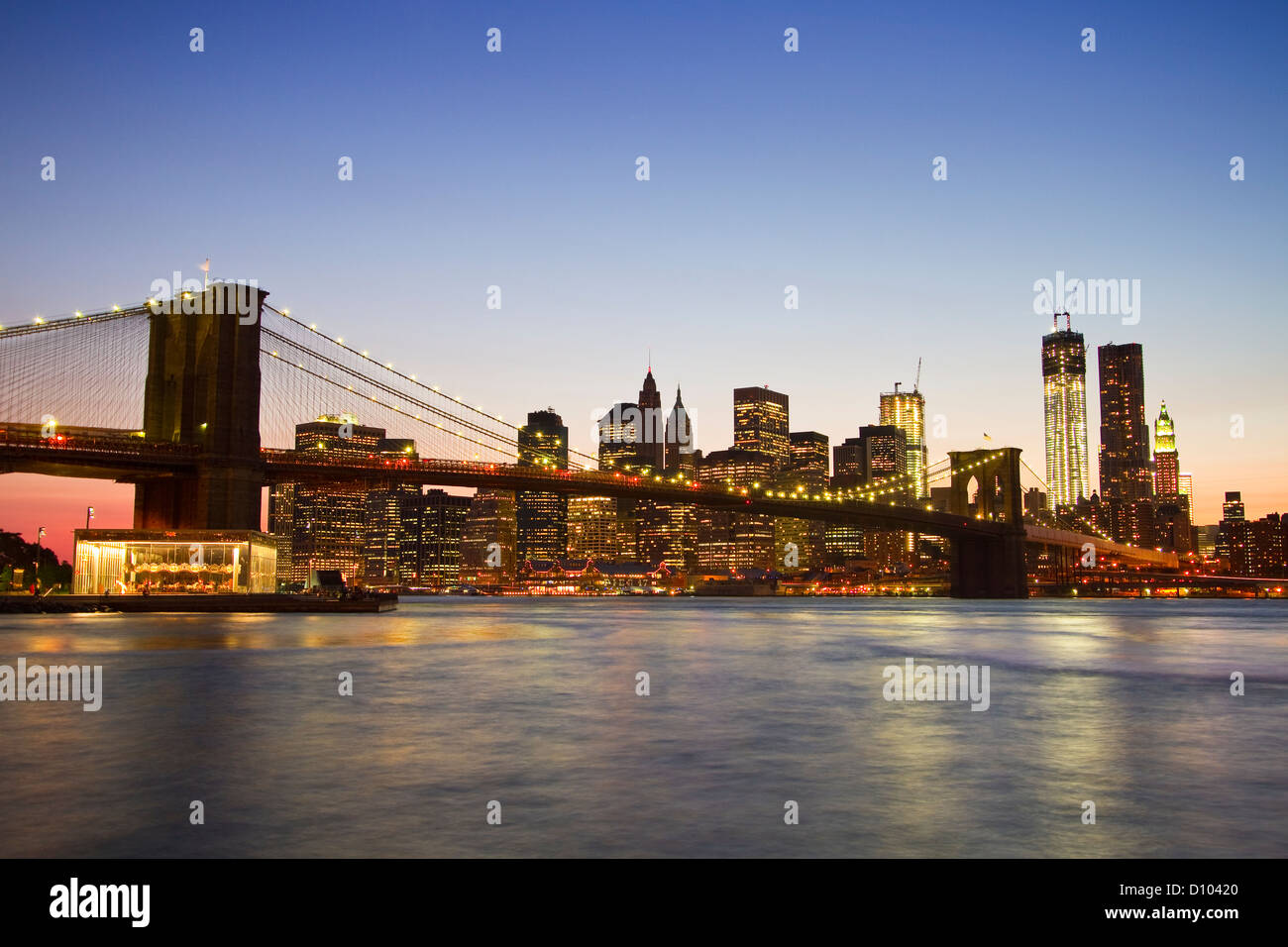 A sunset view of the Brooklyn Bridge and the Manhattan skyline behind ...