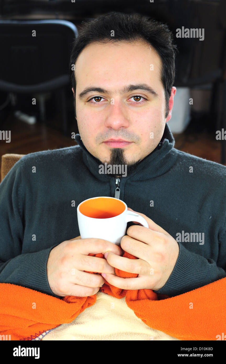 Young man in blanket holding cup of tea Stock Photo