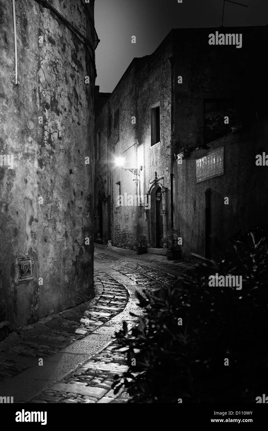 Curved cobblestone street between buildings in Sicily illuminated by street lights Stock Photo