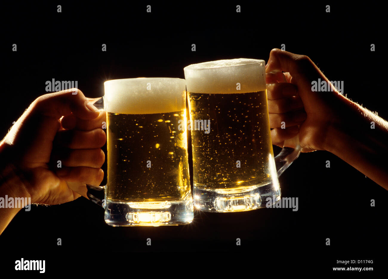 TWO MALE HANDS TOASTING WITH FULL BEER MUGS Stock Photo
