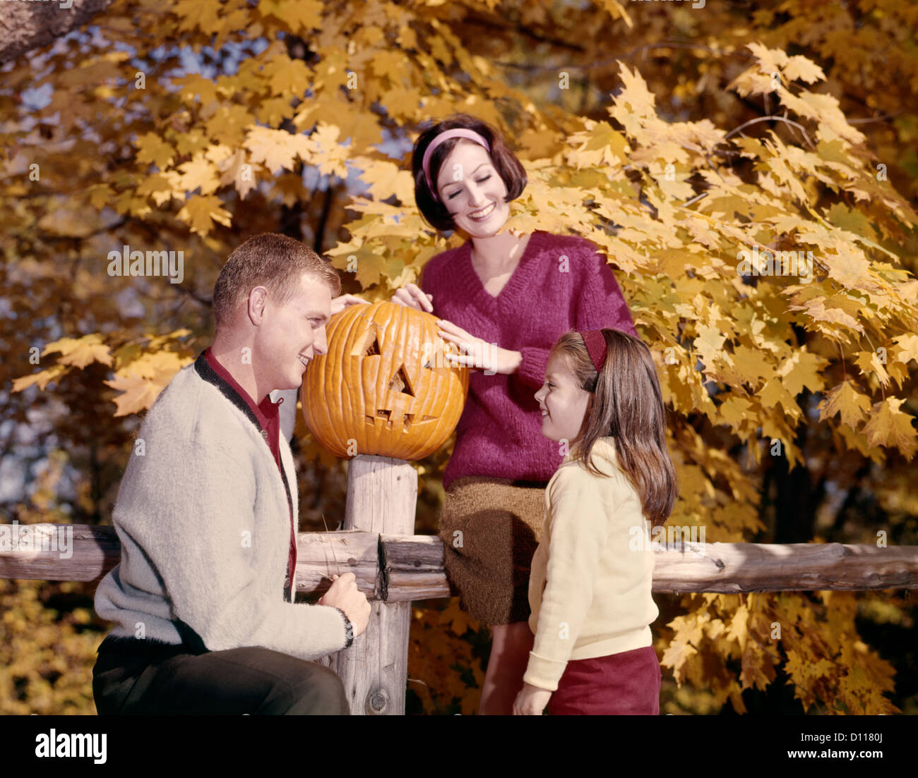 1960s JACK-O'-LANTERN PUMPKIN FAMILY MOTHER FATHER DAUGHTER GIRL FENCE AUTUMN FALL Stock Photo