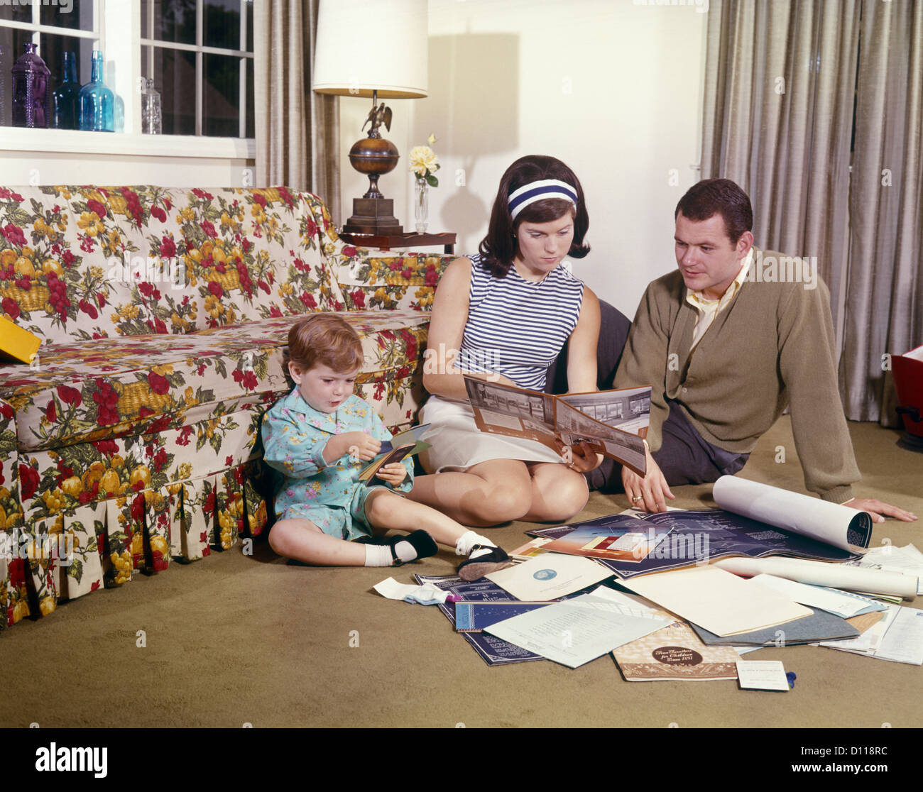 1970s FAMILY MOTHER FATHER DAUGHTER READING BLUEPRINTS PLANS FOR NEW HOME Stock Photo