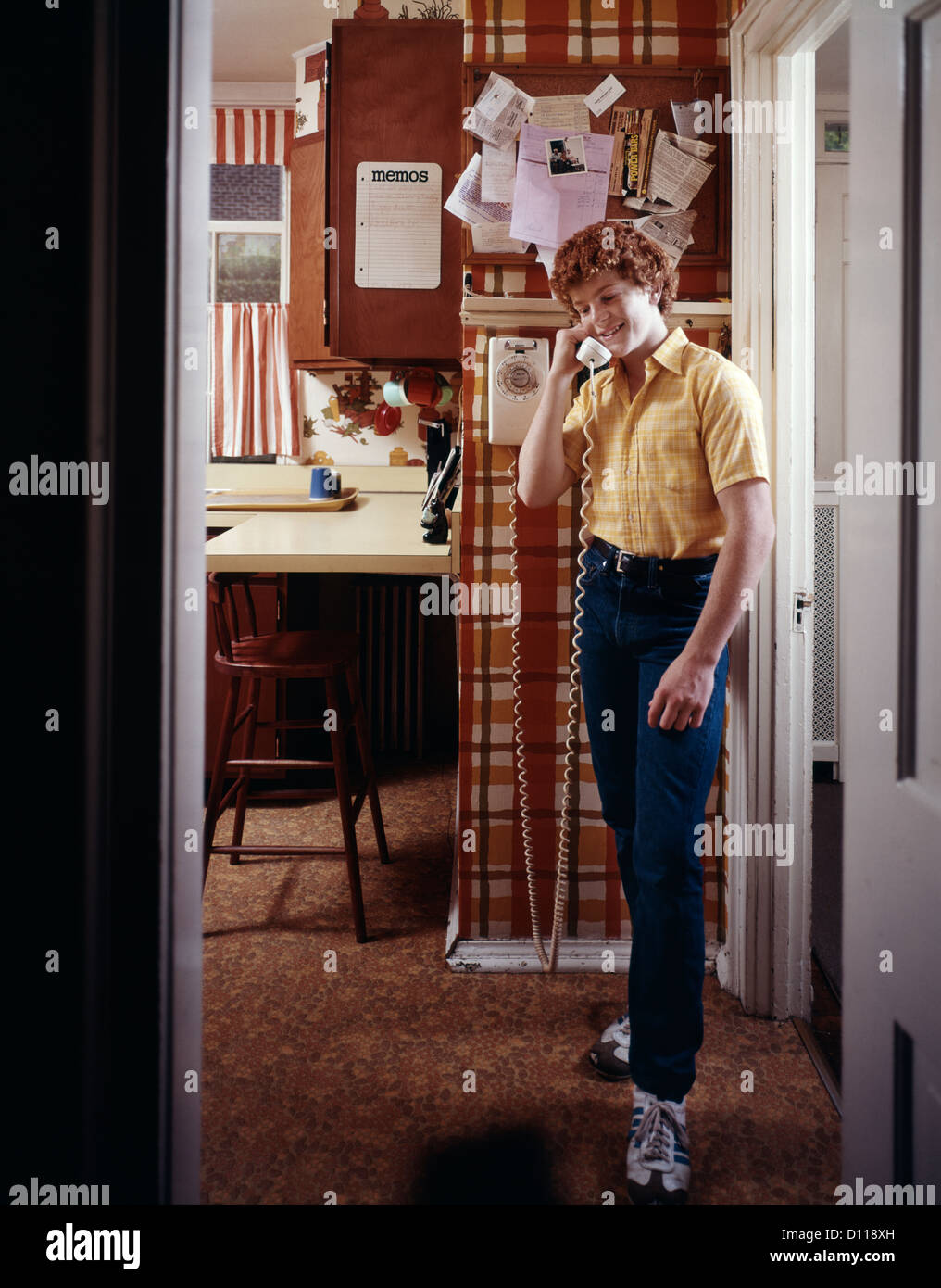 1970s TEENAGE BOY TALKING ON KITCHEN WALL PHONE TELEPHONE Stock Photo
