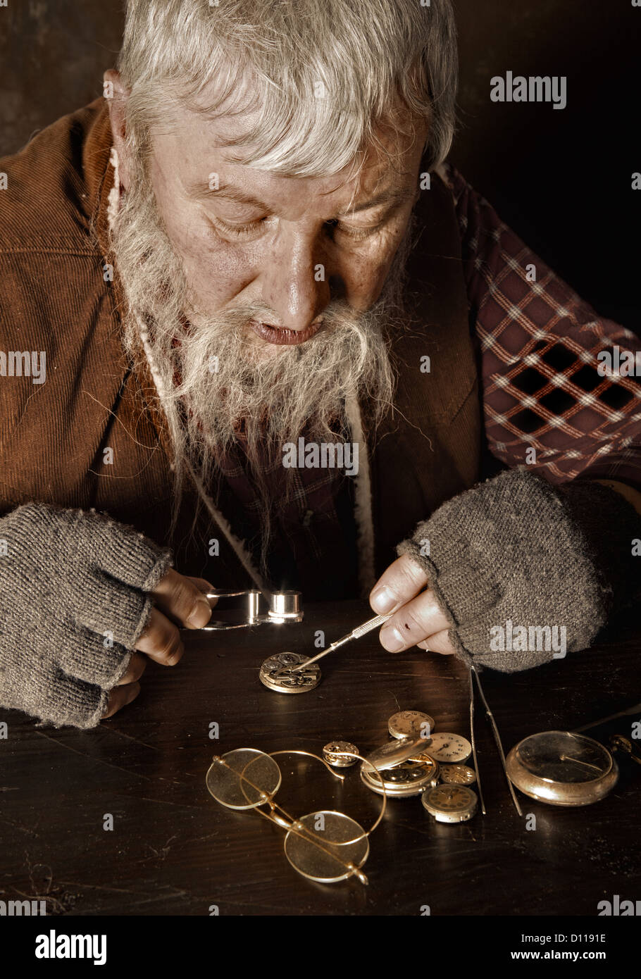 Old bearded man reparing antique watches using a magnifying glass Stock Photo