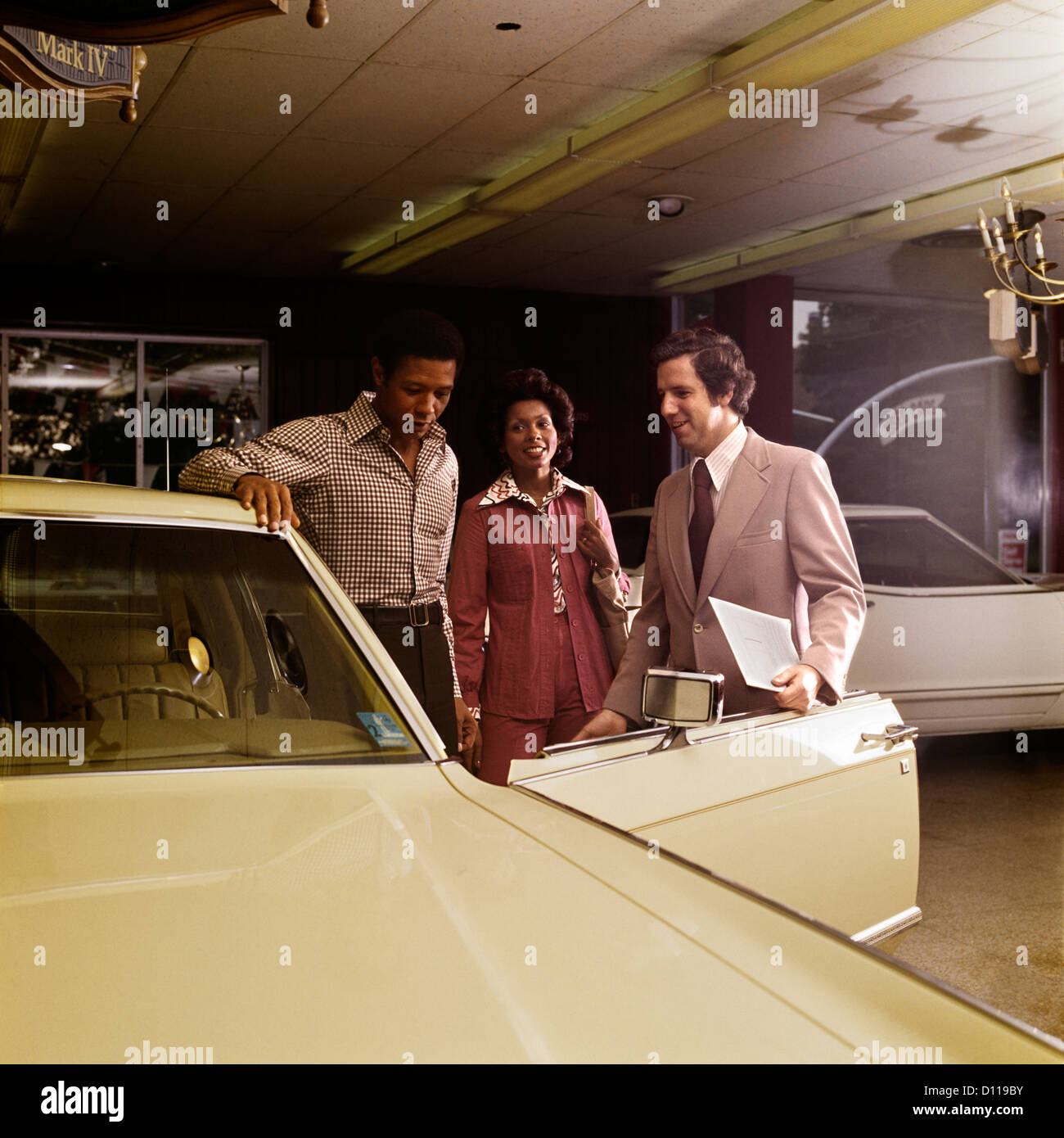 1970s AFRICAN-AMERICAN COUPLE WITH SALESMAN AUTOMOBILE SHOWROOM Stock Photo