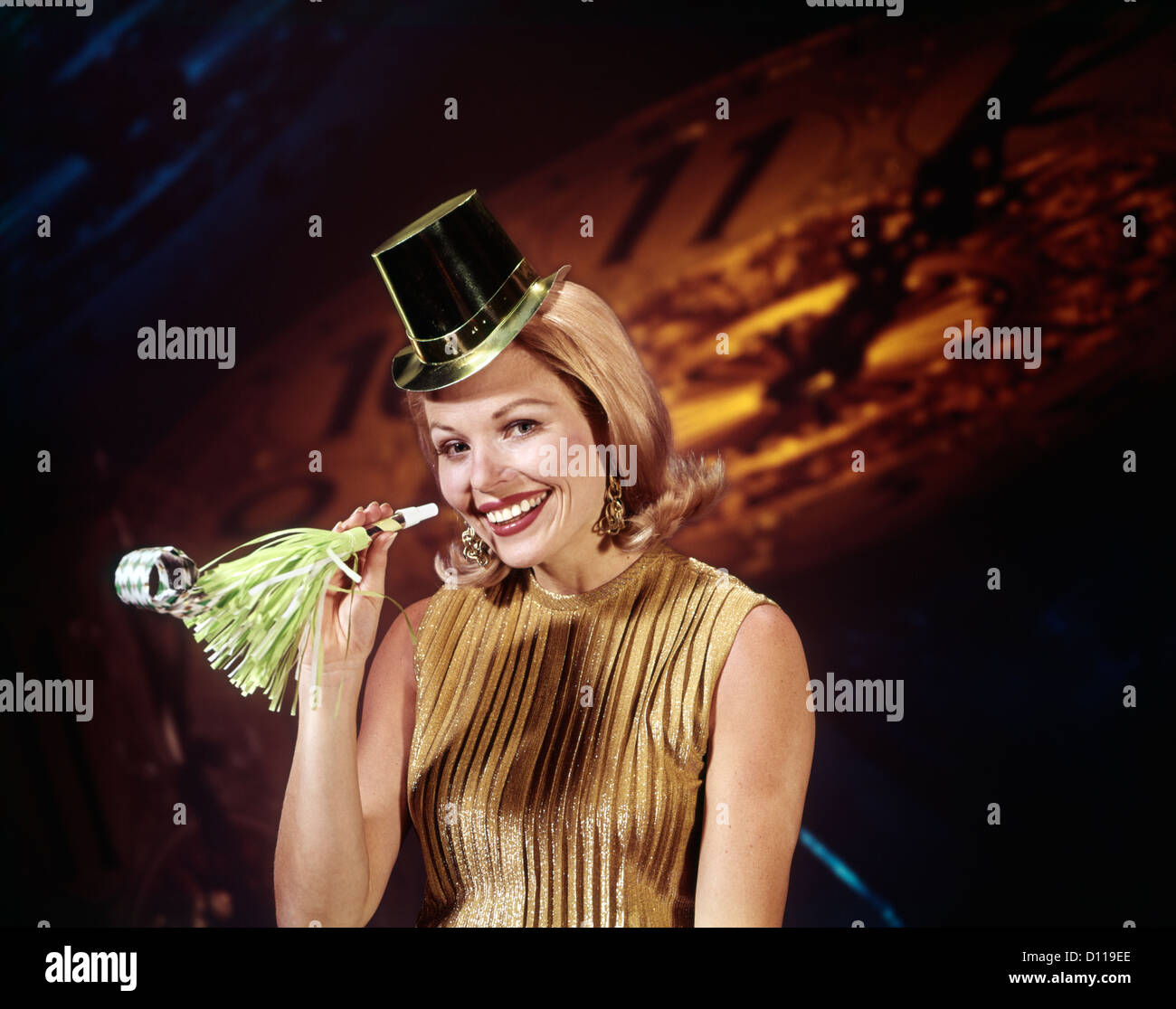 1960s YOUNG BLONDE WOMAN LOOKING AT CAMERA WITH PARTY HAT NOISEMAKER HORN SMILING NEW YEAR CLOCK BACKGROUND Stock Photo