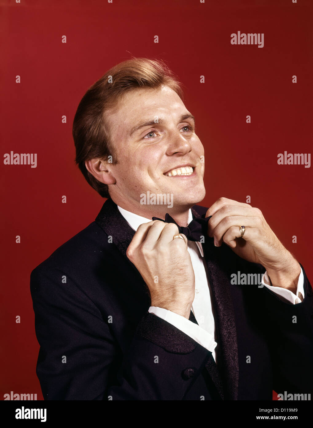 1960s MAN ADJUSTING THE BOW TIE OF HIS TUXEDO Stock Photo
