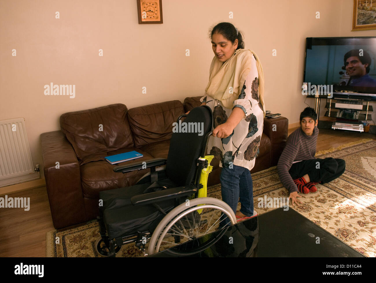 Mother who cares for her 24 year old daughter (seated on floor) with Cerebral palsy moving her wheelchair Stock Photo