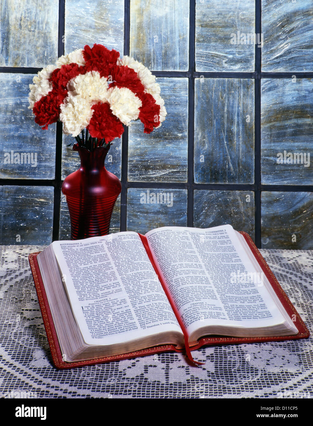 RED AND WHITE CARNATIONS IN RED VASE WITH BIBLE ON TABLE OPEN TO THE