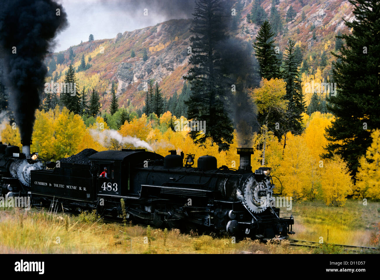 1980s NARROW GAUGE RAILROAD IN AUTUMN CHAMA NM WITH TWO ENGINES TAKING TRAIN UP A GRADE Stock Photo
