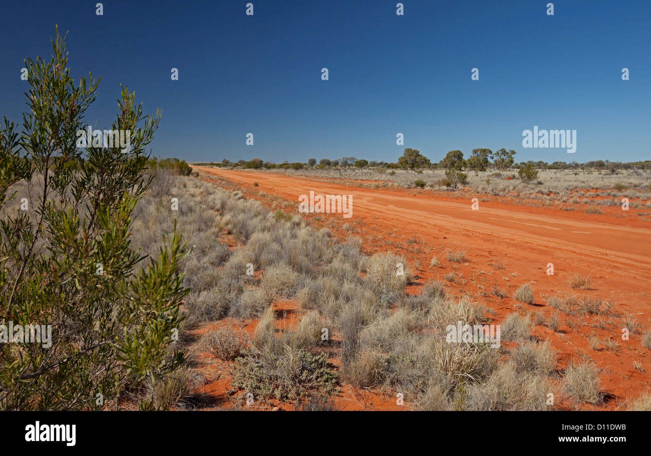 Australian outback road across vast plains and bordered with low native vegetation in outback NSW Australia Stock Photo